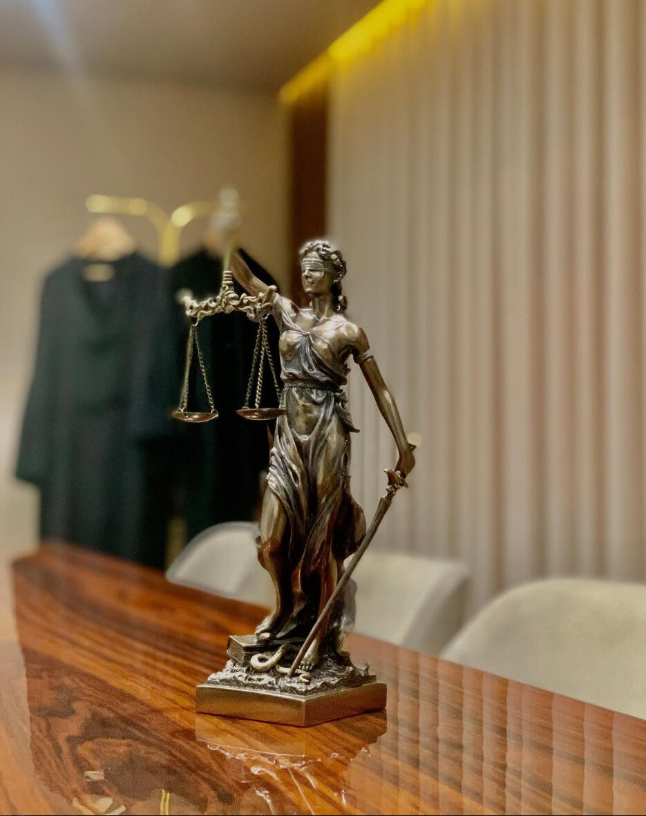 Estátua da Justiça na sala de reuniões da Cunha Advogados, com as togas ao fundo